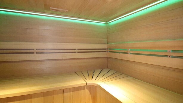 A sauna room with wooden walls and benches, green lighting, and a ceiling light. - Apartment in Netherlands near Nature Trails (Dalerveen)