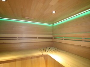 Una sala de sauna con paredes y bancos de madera, iluminación verde y una lámpara en el techo.