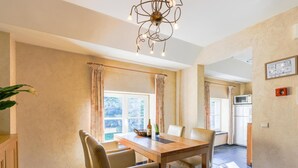 A dining area with a wooden table and chairs, a chandelier, and a view of the kitchen. - Cozy apartment in a 16th-century castle (Aywaille)