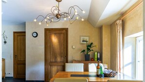 A dining area with a wooden table, beige chairs, a chandelier, and a potted plant. - Cozy apartment in a 16th-century castle (Aywaille)