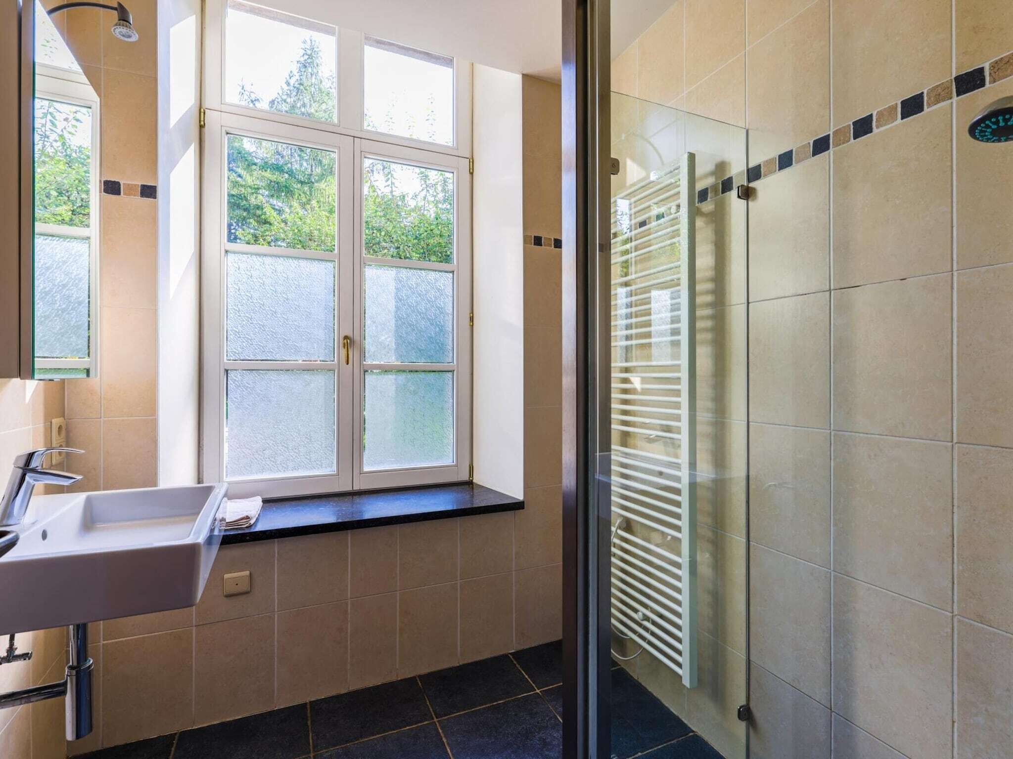 A modern bathroom with a window, a sink, and a glass shower enclosure.