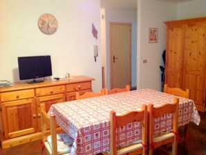 A dining area with a table set for four, a television on a wooden cabinet, and a door leading to another room.