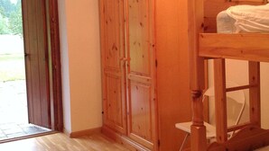 A room with a wooden wardrobe, a bed, and a door leading outside.