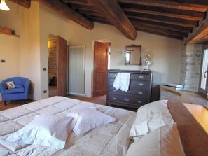 A bedroom with a large bed, a dresser, a chair, and a stone wall. - Belvilla by OYO La Rocca (Apecchio)