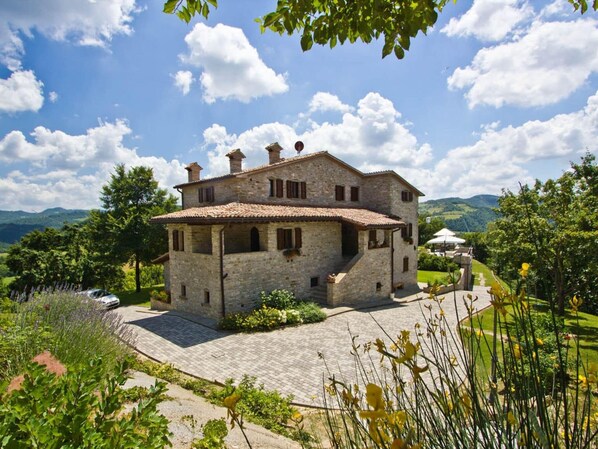 A stone house with a tiled roof, surrounded by a garden and a paved driveway. - Belvilla by OYO La Rocca (Apecchio)