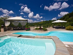 A swimming pool with a pergola and lounge chairs, surrounded by stone tiles and greenery. - Belvilla by OYO La Rocca (Apecchio)