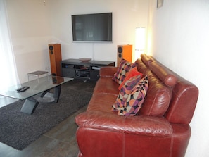 A modern living room with a glass coffee table, leather sofa, and a flat-screen TV mounted on the wall.