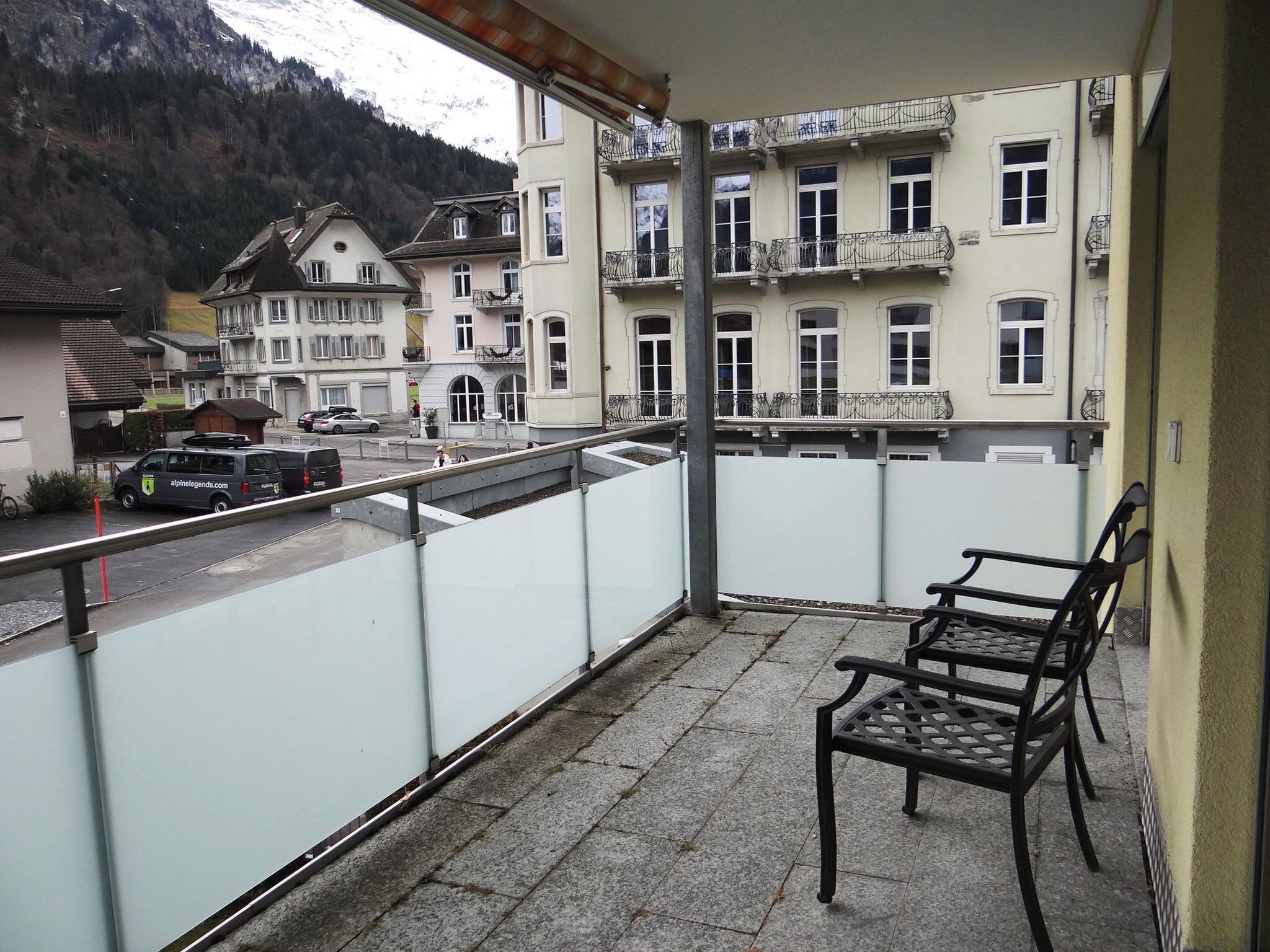 A balcony with a view of a mountain, a parked car, and a building with multiple windows and balconies.