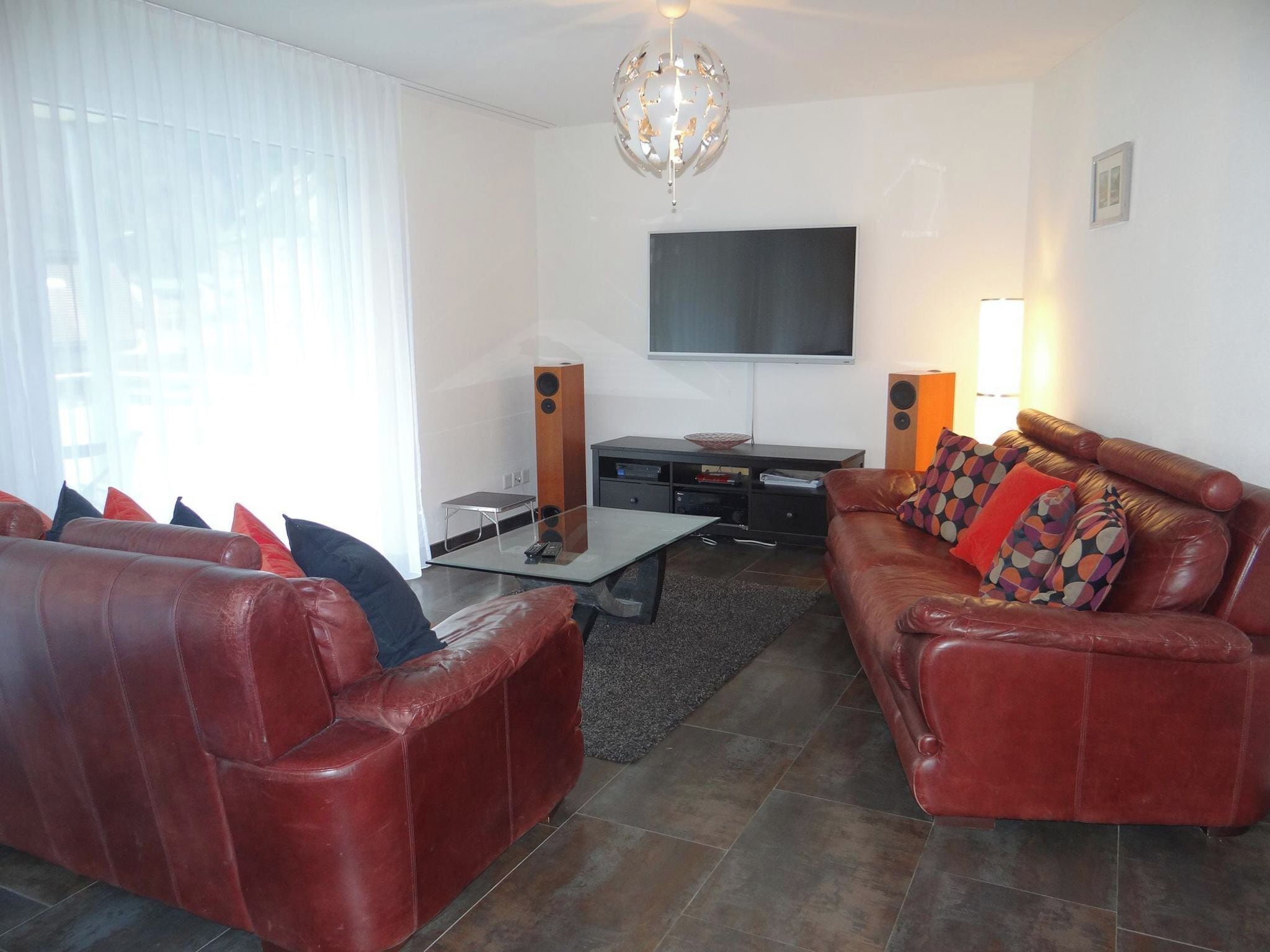 A living room with leather sofas, a coffee table, a flat-screen TV, and speakers.