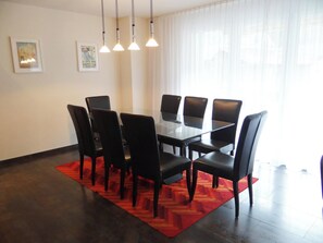 A dining area with a glass table surrounded by chairs, a red rug, and pendant lights.
