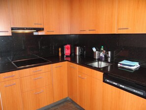 A kitchen with wooden cabinets, a black countertop, a dishwasher, and various kitchen appliances. - Bellevue-Park B 145 Appartement/Fewo 6-Bettwohnung by Interhome (Engelberg)