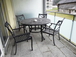 A round metal table with four chairs on a balcony with a view of a building and a house.
