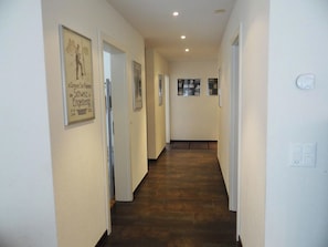 A hallway with framed pictures on the walls, a wooden floor, and a light switch on the right.