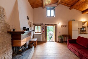 A rustic interior with a fireplace, stone walls, a red sofa, and a kitchen area. - Country House with Saltwater Pool (Acqualagna)