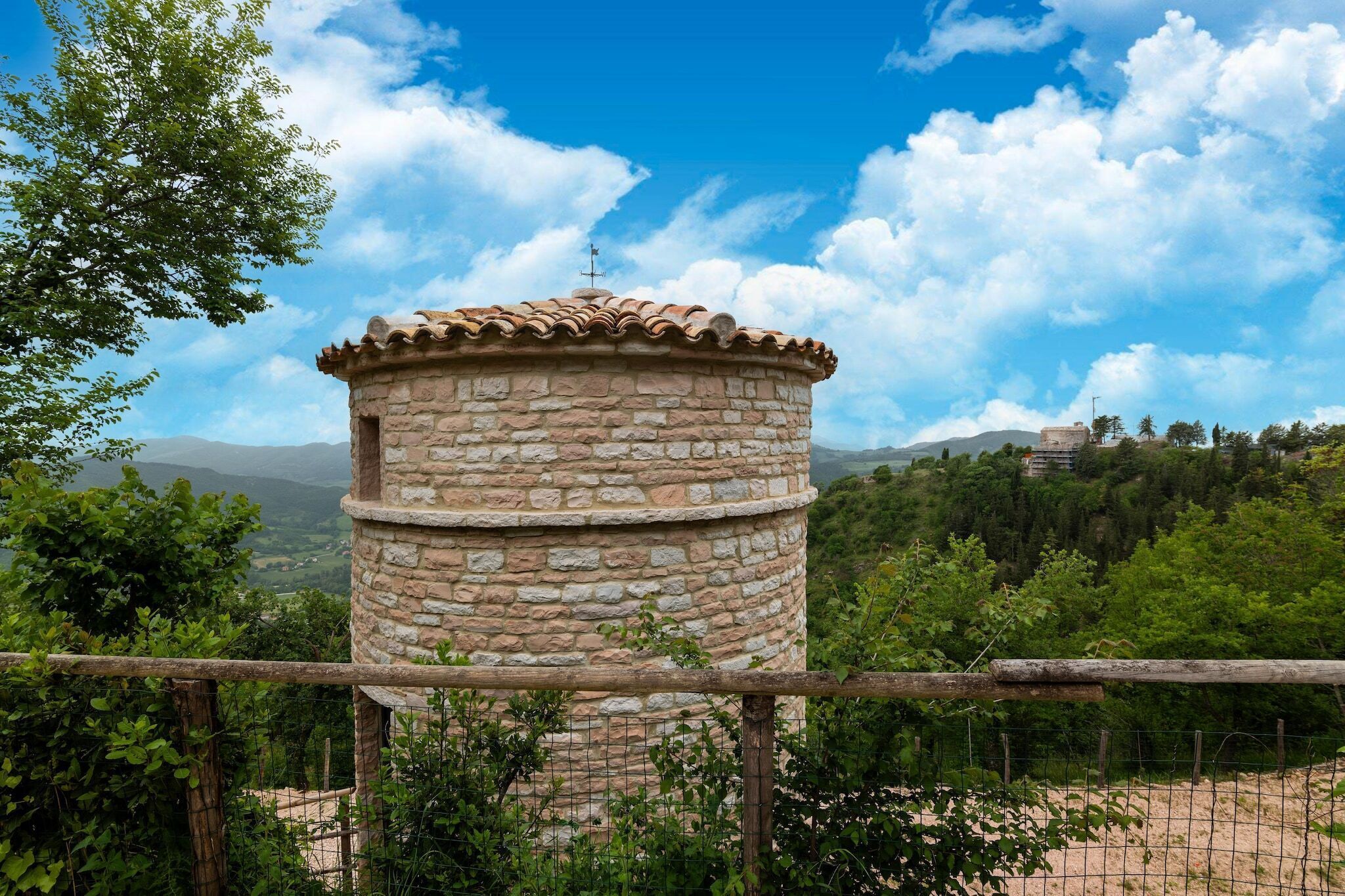 A stone tower with a tiled roof, surrounded by greenery and a clear sky.