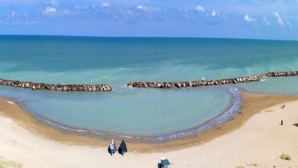 Una playa con aguas cristalinas, una costa curva y un rompeolas rocoso.