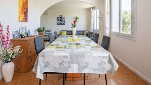 A dining area with a long table covered in a patterned tablecloth, flanked by chairs, a wooden cabinet, and a vase with flowers. - Pretty holiday home with garden and hot tub (Bédoin)