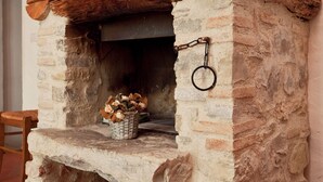A stone fireplace with a wooden mantel, a basket of firewood, and a metal ring on the wall. - Idyllic Tuscan Hideaway with Pool and spa (Montorsoli)