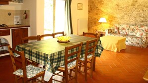 A cozy dining area with a table set for four, wooden chairs, a floral sofa, and a kitchen area with a stove and counter. - Idyllic Tuscan Hideaway with Pool and spa (Montorsoli)