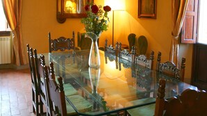 A dining area with a glass table surrounded by wooden chairs, a vase with flowers, and a lamp on the wall. - Villa Life in Vicchio; the Tuskan way (Vicchio)