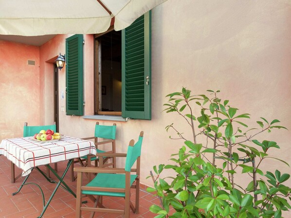 An outdoor patio with a table set for two, green chairs, a tablecloth, and a potted plant.