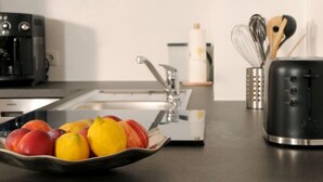 Eine Küche mit Spüle aus Edelstahl, einer Kaffeemaschine, einem Toaster und einer Obstschale auf der Arbeitsfläche.