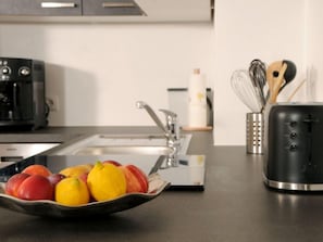 A kitchen with a stainless steel sink, a coffee maker, a toaster, and a bowl of fruit on the counter.