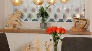 Ein Essbereich mit einem Holztisch, dekorativen Holzfiguren und einer Vase mit roten Blumen.