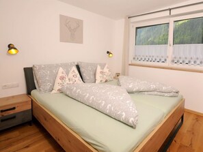A bedroom with a bed, pillows, a nightstand, a wall-mounted lamp, and a window with curtains.