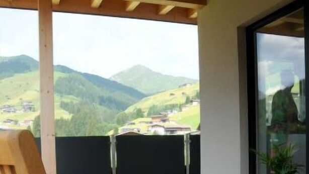 Ein Balkon mit Holzstühlen und einem Tisch, mit Blick auf eine gebirgige Landschaft.