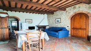Un intérieur rustique avec un mur en pierre, des poutres en bois au plafond, une table à manger avec des chaises, un canapé bleu et une porte en bois.