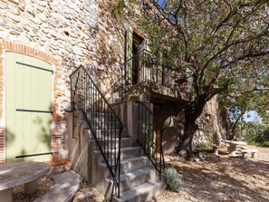 A stone building with a green door, a staircase with black railings, and a tree in the background. - Holiday Home in Tautavel near Gorges de Gouleyrous (Tautavel)