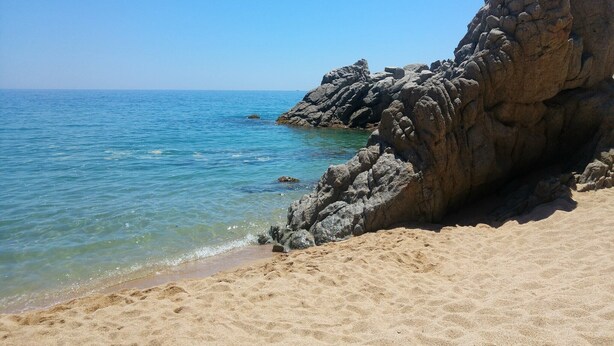 Una playa arenosa con una gran formación rocosa y aguas azules tranquilas.