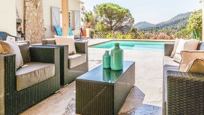 Un área de estar al aire libre techada con mobiliario de mimbre y una piscina.