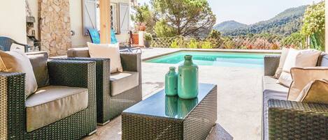 A covered outdoor seating area with wicker furniture and a pool.