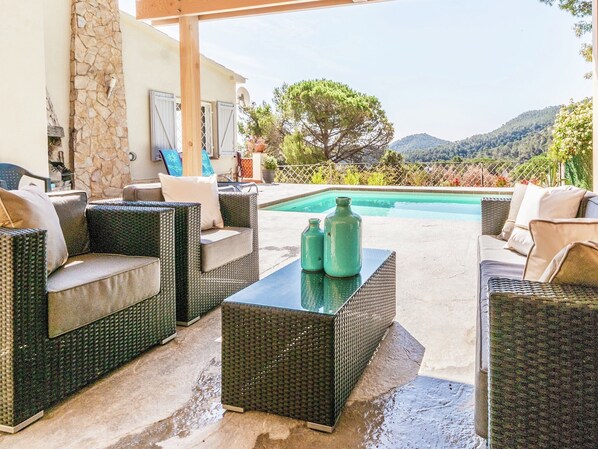A covered outdoor seating area with wicker furniture and a pool.