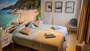 Un dormitorio con dos camas, una mesita de noche, una silla y un amplio mural de playa en la pared.