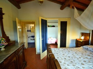 Ein Schlafzimmer mit einem hölzernen Bett, einem Nachttisch, einer Kommode und einem durch eine offene Tür einsehbaren Badezimmer.
