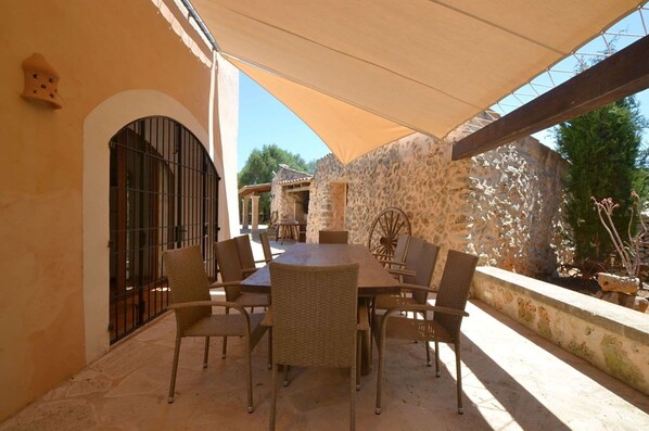 An outdoor patio with a round table and wicker chairs, a stone wall, and a covered area with a canopy. - Countryside Villa & Garden (Felanitx)