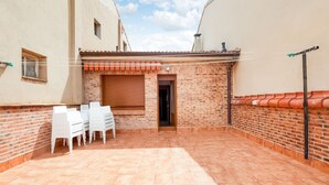 A covered patio area with a brick wall, a tiled floor, and a set of white chairs. - Stay in Historic Laguardia, Sleeps 8 (Laguardia)