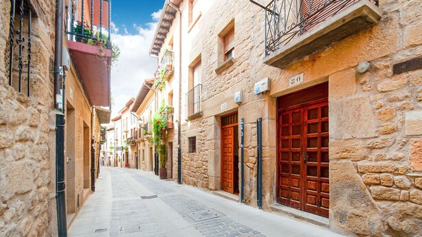 A narrow cobblestone street flanked by stone buildings with wooden doors and balconies. - Stay in Historic Laguardia, Sleeps 8 (Laguardia)