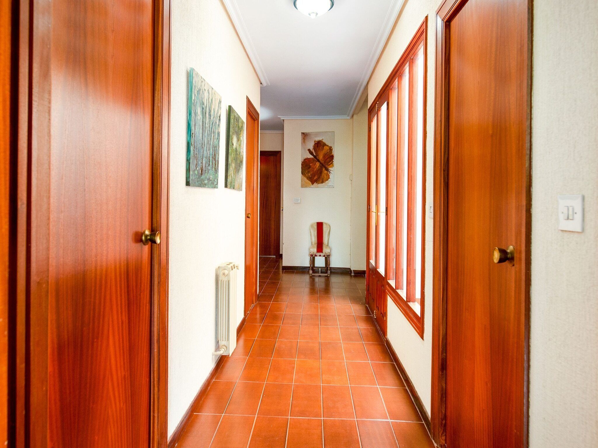 Un corridoio con porte in legno, pavimento piastrellato e opere d'arte alle pareti.