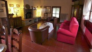 A cozy living room with a stone fireplace, a red sofa, and a dining table. - Quaint cottage with pool (Anghiari)