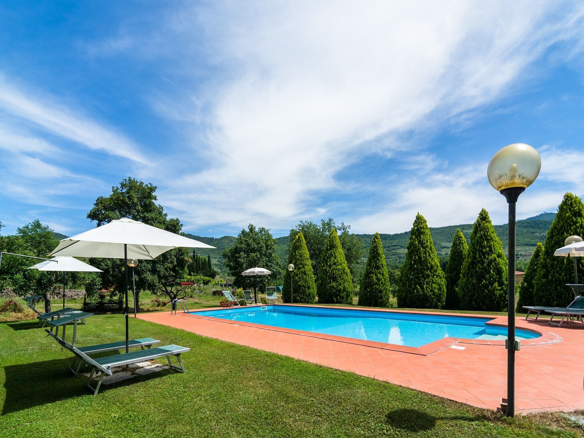 Une piscine entourée de chaises longues et de parasols, avec une végétation luxuriante et des collines en arrière-plan.
