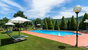Une piscine entourée de chaises longues et de parasols, avec une végétation luxuriante et des collines en arrière-plan.