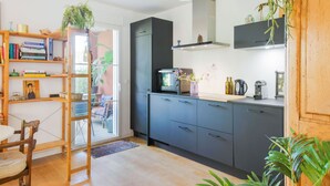 A modern kitchen with dark cabinets, a wooden chair, a bookshelf, and a hanging plant.