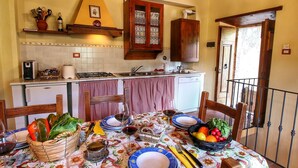 A cozy kitchen with wooden cabinets, a dining table set with plates, glasses, and a fruit basket. - Apartment in Radda with Garden (Radda in Chianti)