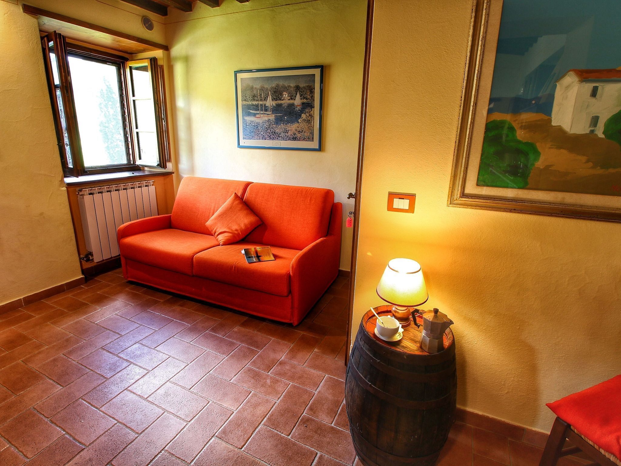 A cozy room with a red sofa, a wooden barrel with a lamp, and a painting on the wall.