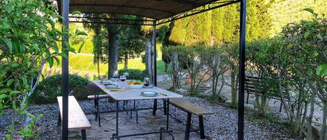 An outdoor patio with stone flooring, metal tables, and benches under a pergola.