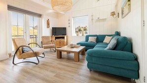 A spacious living room with a teal sofa, a wooden coffee table, a wicker pendant light, and a TV on a wooden cabinet. - Top location! Next to lighthouse, beach 50m SIGHT (Egmond aan Zee)